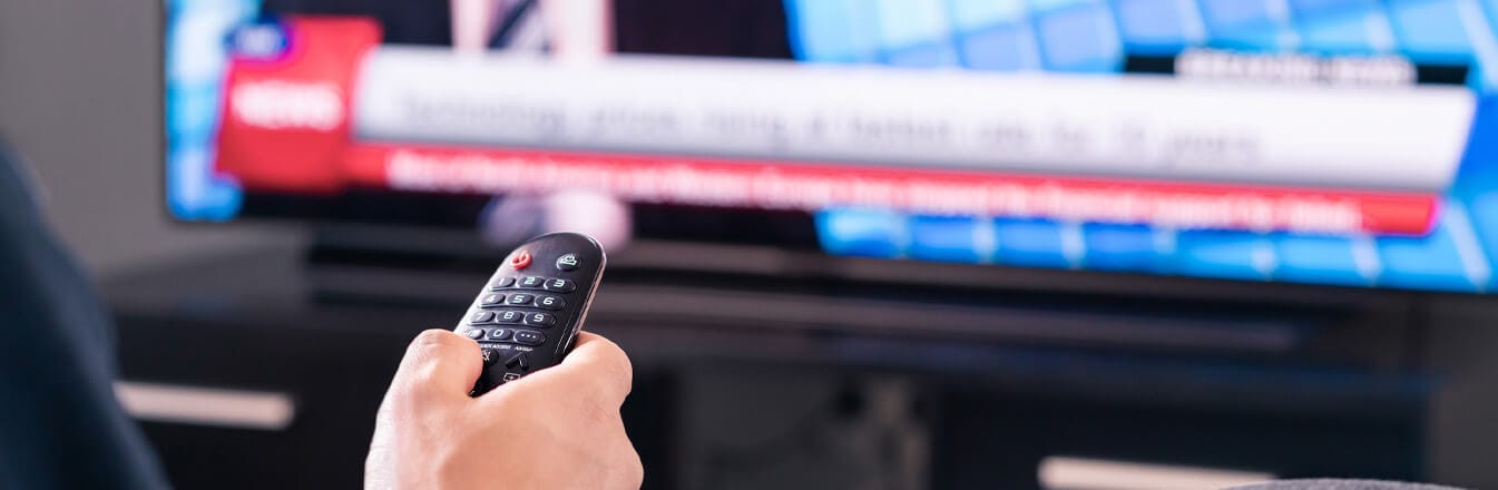 Hand holding remote to TV which is showing a news channel